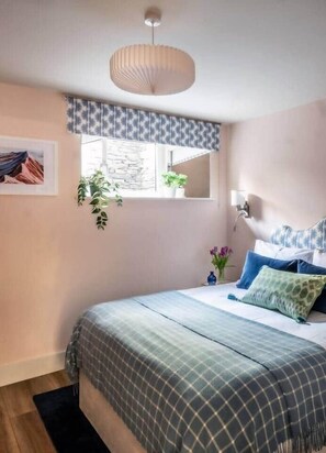 A bedroom with a bed, a window with a view, a hanging light fixture, and a wall-mounted plant.