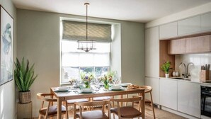 A modern kitchen with a dining area, featuring a large window, wooden furniture, and a hanging light fixture. - Bracken House - Luxury design 3 bed in Windermere (Windermere)