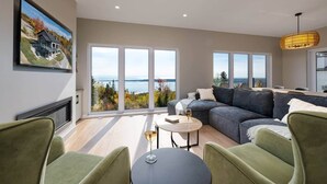 Ein modernes Wohnzimmer mit einer großen Eckcouch, einem runden Couchtisch und Meerblick durch raumhohe Fenster.