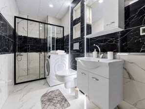 Un bagno moderno con cabina doccia in vetro, lavatrice integrata, lavandino con specchio e pavimento in marmo.