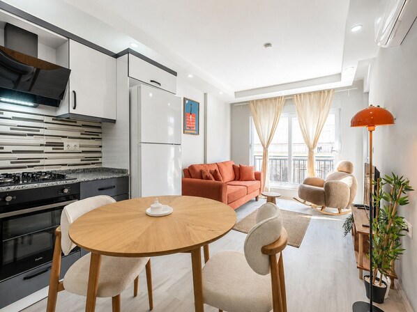 Una cucina moderna con piano cottura a gas, frigorifero e zona pranzo con tavolo rotondo in legno e sedie.