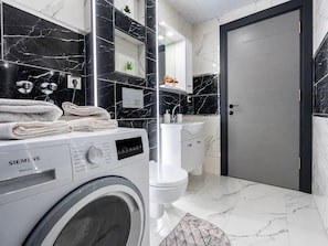 A modern bathroom with a Siemens washing machine, a toilet, a sink, and a door.