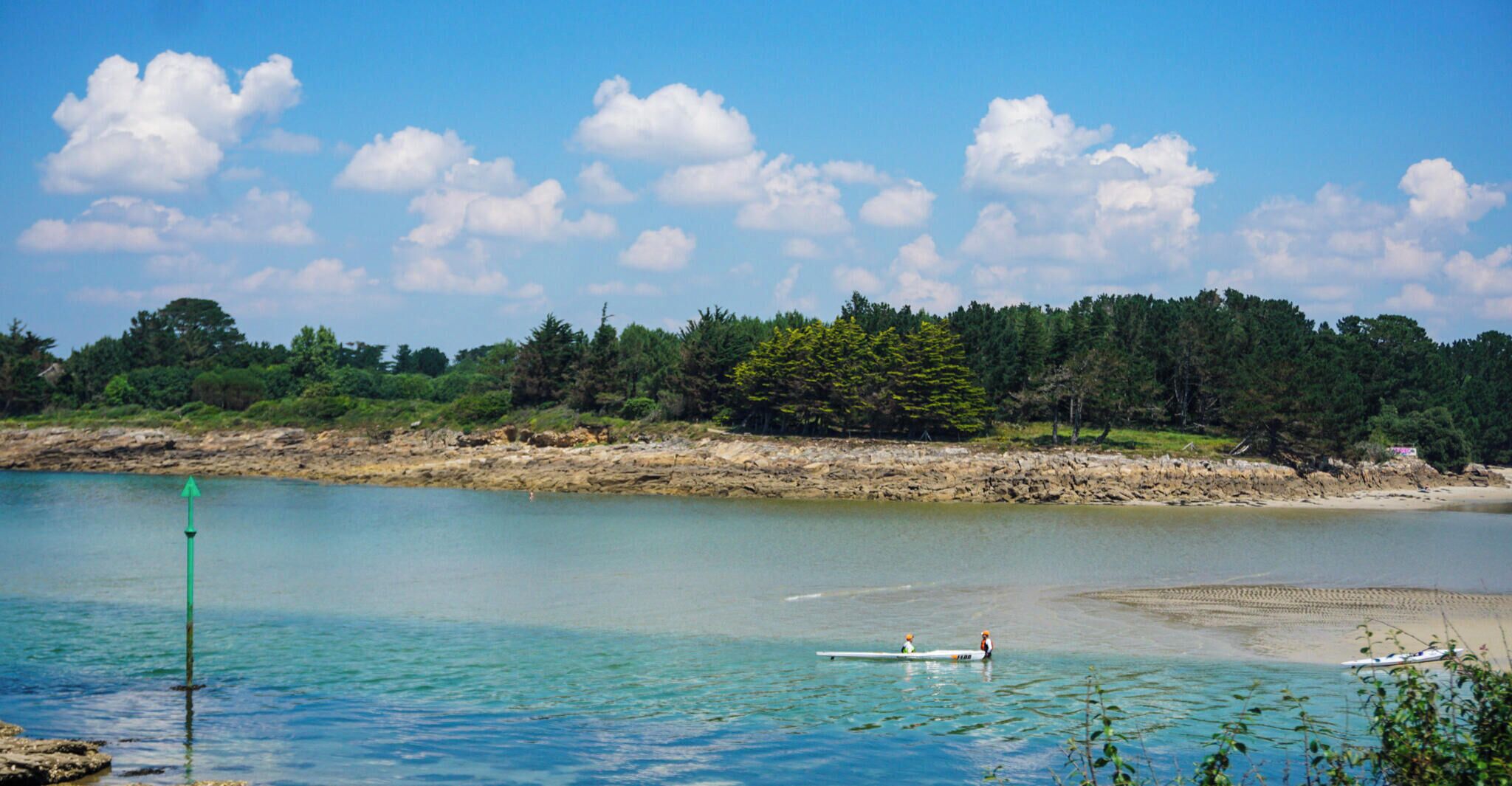 Un lago tranquilo con barcos, una costa rocosa y un bosque al fondo.