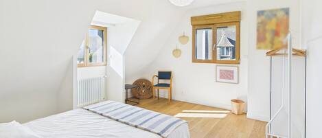 Un dormitorio con cama, una silla, una mesita, una ventana y un radiador.