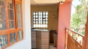 A room with a kitchen area, a window with a grid pattern, and a balcony with a wooden railing.