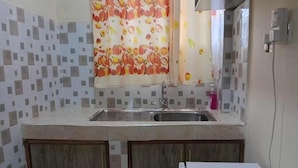 A kitchen with a tiled backsplash, a stainless steel sink, wooden cabinets, and a white countertop.