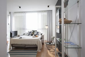 Une chambre moderne avec un lit, une table de chevet, une télévision et une étagère en verre où sont posés des livres.