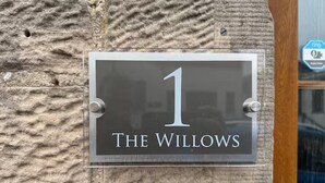 A house number sign with "1" and "The Willows" on a textured stone wall.