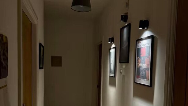 A hallway with a black pendant light, a framed picture, and a poster on the wall.