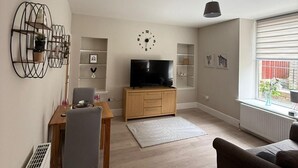 A living room with a TV, wooden furniture, a radiator, and a window with a view.