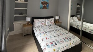 A bedroom with a bed, bedside tables, a mirror, a shelf with model houses, and a painting of a horse.