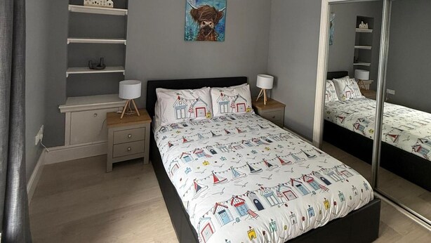 Ett sovrum med en säng, sängbord, en spegel, en hylla med modellhus och en tavla som föreställer en häst.