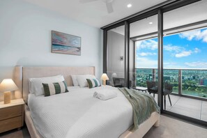 Ein modernes Hotelzimmer mit einem großen Bett, Blick auf die Stadt durch raumhohe Fenster und einem Sitzbereich auf dem Balkon.