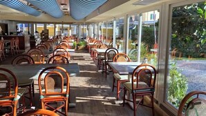 Ein Restaurant mit Holztischen und -stühlen, großen Fenstern und einer Decke mit blauen und weißen Streifen.