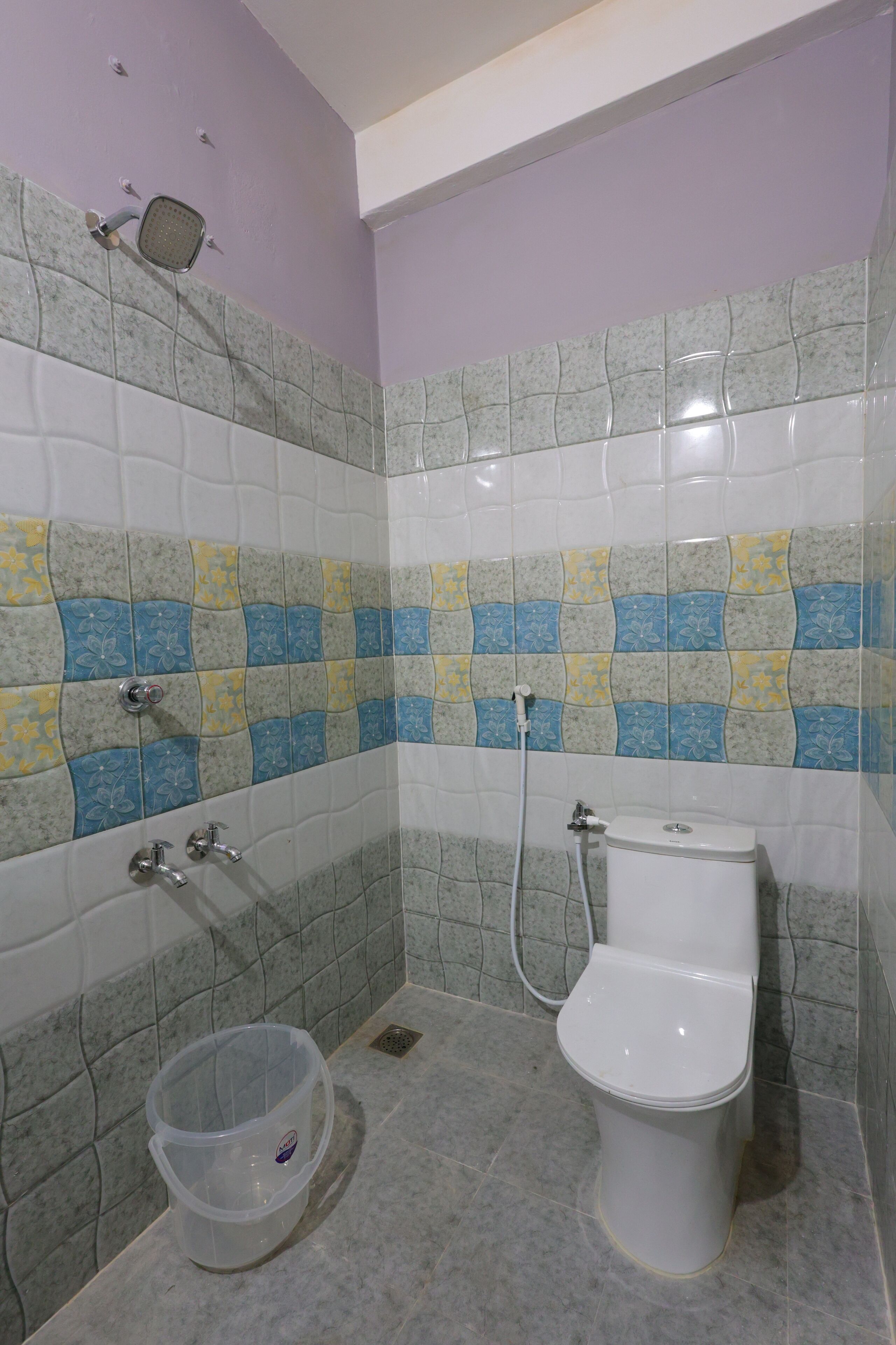 A bathroom with a toilet, shower, and a plastic container on the floor.