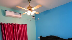 A bedroom with a bed, a ceiling fan, a red curtain, and an air conditioning unit. - Nautical Escape Homestay - Pondicherry (Puducherry)