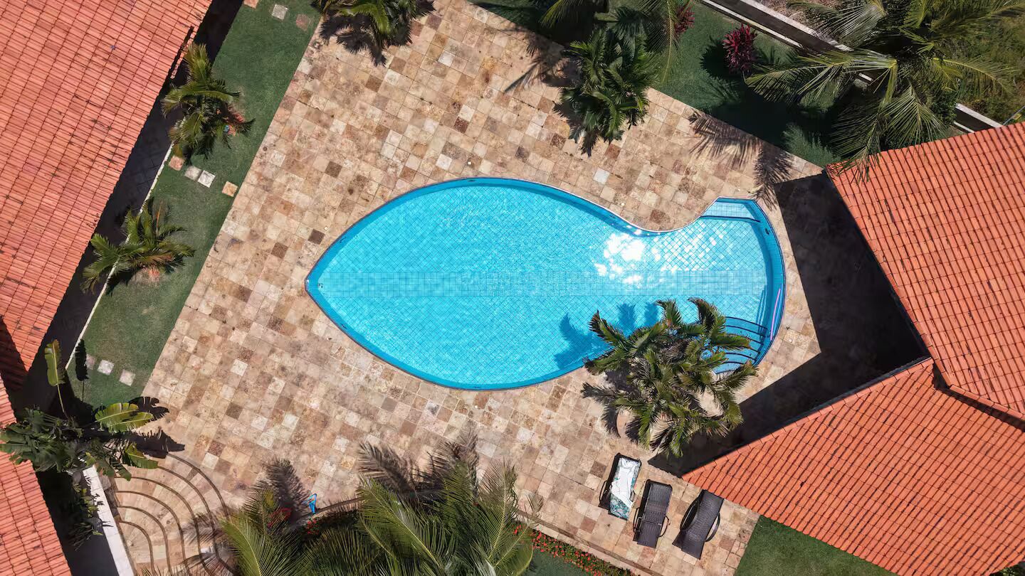 Piscina en la azotea con forma de corazón, rodeada de palmeras y un solárium de baldosas a cuadros.