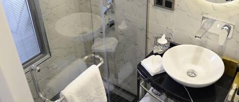A bathroom with a glass-enclosed shower, a white sink, and a marble-tiled wall.