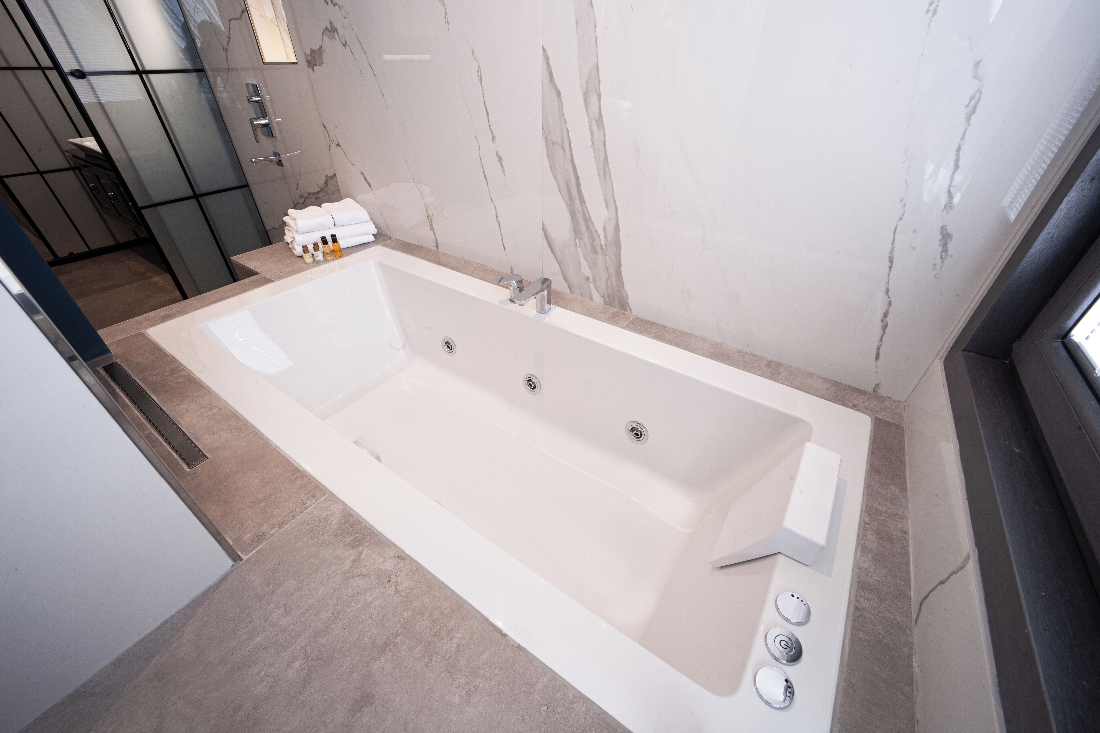 A modern bathroom with a large bathtub, a shower area, and a marble wall.