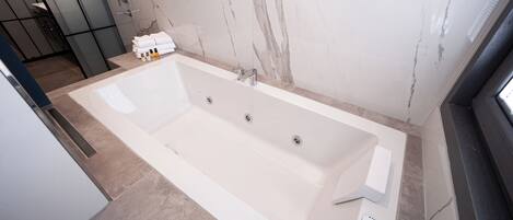 A modern bathroom with a large bathtub, a shower area, and a marble wall.