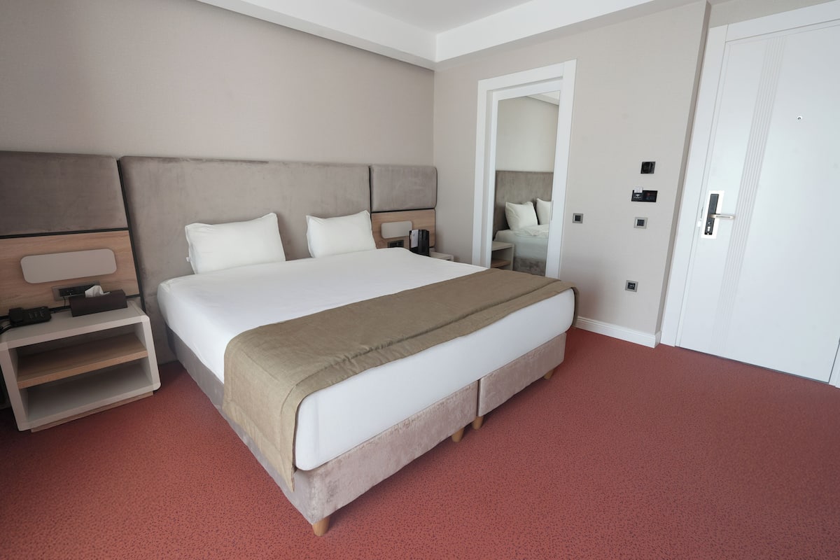 A neatly arranged hotel room with a large bed, a bedside table with a lamp, and a wardrobe.