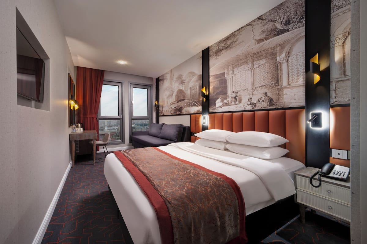 A hotel room with a large bed, a desk, a chair, and a view of the city.
