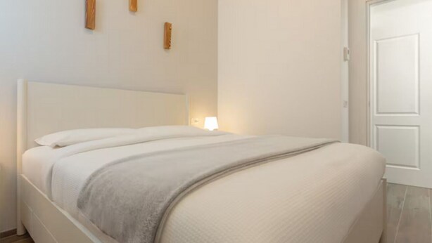 A neatly made bed with a white headboard, a grey blanket, and a small bedside lamp. - Flower apartment - new bright home in Brera (milano)