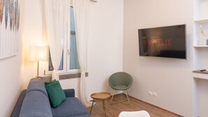 A modern living room with a grey sofa, a green pillow, a small round table, a green chair, and a TV mounted on the wall displaying the Netflix logo. - Flower apartment - new bright home in Brera (milano)