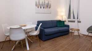 A modern living room with a blue sofa, white chairs, a round dining table, and a small side table. - Flower apartment - new bright home in Brera (milano)