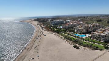 Un complejo turístico frente al mar con playa, piscina y edificios residenciales.