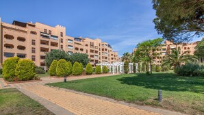 A courtyard with a paved walkway, neatly trimmed hedges, and a building with balconies and windows. - Apartment 'Albatros' with Shared Pool, Private Terrace and Wi-Fi (Ayamonte)