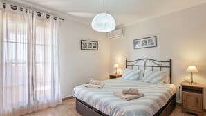 A bedroom with a bed, two bedside tables with lamps, a window with sheer curtains, and wall-mounted air conditioning. - Apartment 'Albatros' with Shared Pool, Private Terrace and Wi-Fi (Ayamonte)