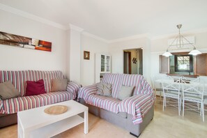 A living room with a striped sofa, a white coffee table, and a dining area with a white table and chairs. - Apartment 'Albatros' with Shared Pool, Private Terrace and Wi-Fi (Ayamonte)
