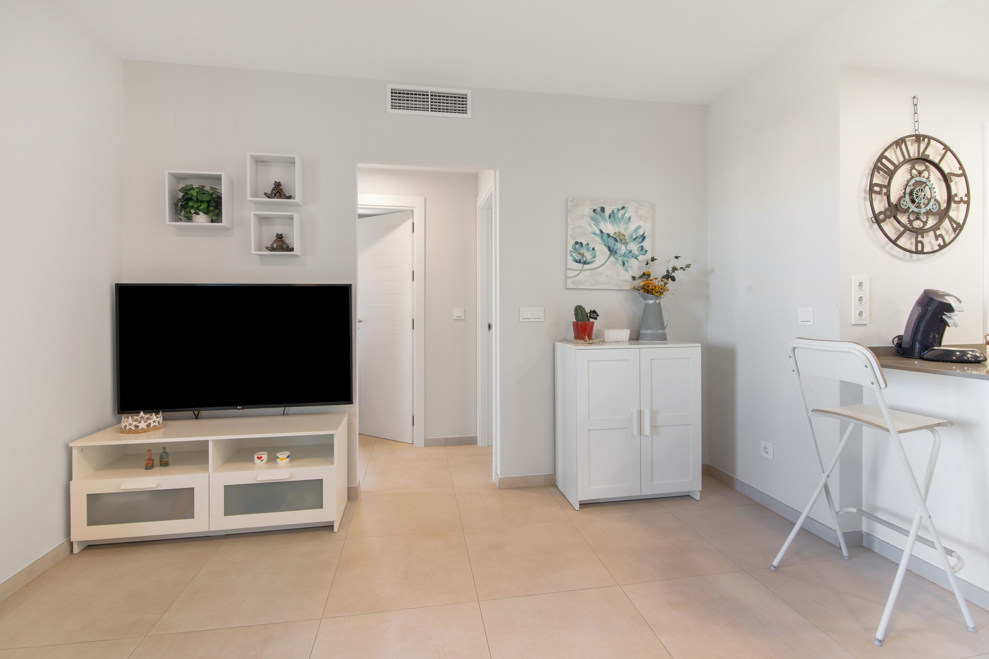 A modern living room with a flat-screen TV, white cabinetry, a small plant, and a clock on the wall.