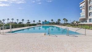 A swimming pool with a clear blue sky, palm trees, and a modern building in the background. - Apartment 'Los Flamencos' with Sea View, Wi-Fi and Air Conditioning (Isla Canela)