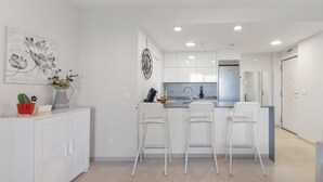 A modern kitchen with white cabinets, a central island with bar stools, and a dining table. - Apartment 'Los Flamencos' with Sea View, Wi-Fi and Air Conditioning (Isla Canela)