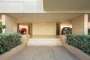 A building entrance with a paved pathway leading to a set of stairs, flanked by greenery.