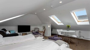 Una camera moderna e luminosa con un letto grande, una televisione, un tavolino con sedie e lucernari.