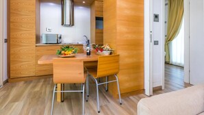 A compact kitchen with wooden cabinetry, a stainless steel range hood, and a dining area with two chairs and a table. -  Hotiday Lodge Cecina (Cecina)