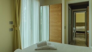 A hotel room with a bed, a wooden wardrobe, a bathroom with a sink, and a mirror. -  Hotiday Lodge Cecina (Cecina)