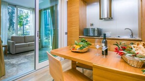 A modern kitchen with a wooden table, a built-in oven, and a large window overlooking a garden. -  Hotiday Lodge Cecina (Cecina)