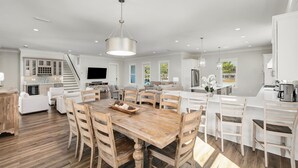 A spacious kitchen with a central island, white cabinetry, and a dining area with wooden chairs. - Rising Tide | Private Pool/Spa | 6-Seater Golf Cart | Private Beach Access (Miramar Beach)