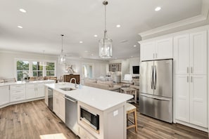 A spacious kitchen with white cabinetry, a large island, stainless steel appliances, and pendant lighting.