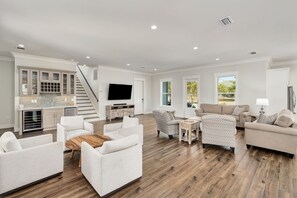 A spacious living room with a kitchen area, a staircase, and a large window providing natural light.