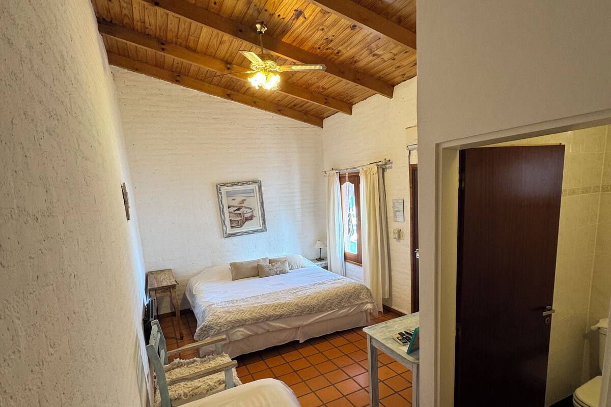 Une chambre avec un plafond en bois, un lit, une petite table et une porte donnant sur une salle de bain.