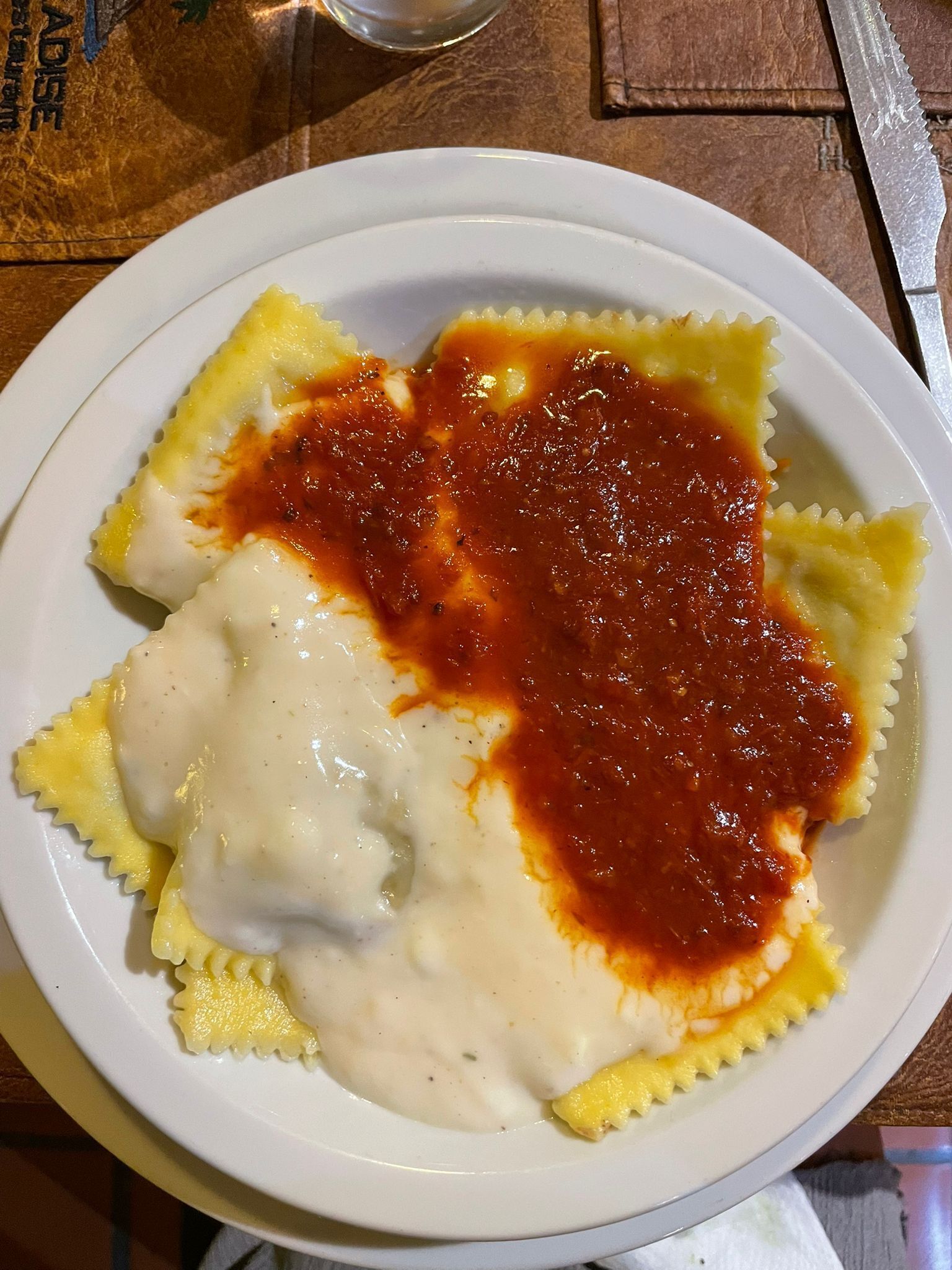 A plate of ravioli with tomato sauce and a creamy sauce on a white plate.