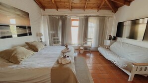A hotel room with a large bed, a sofa, a TV, and a window with curtains. - The Paradise (Puerto Piramides)
