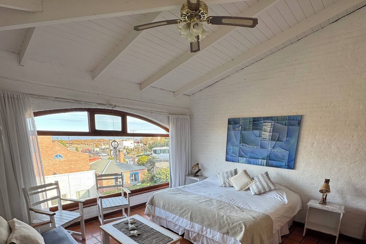 Une chambre à coucher comprenant un lit, un bureau, une chaise, une fenêtre et un ventilateur de plafond.