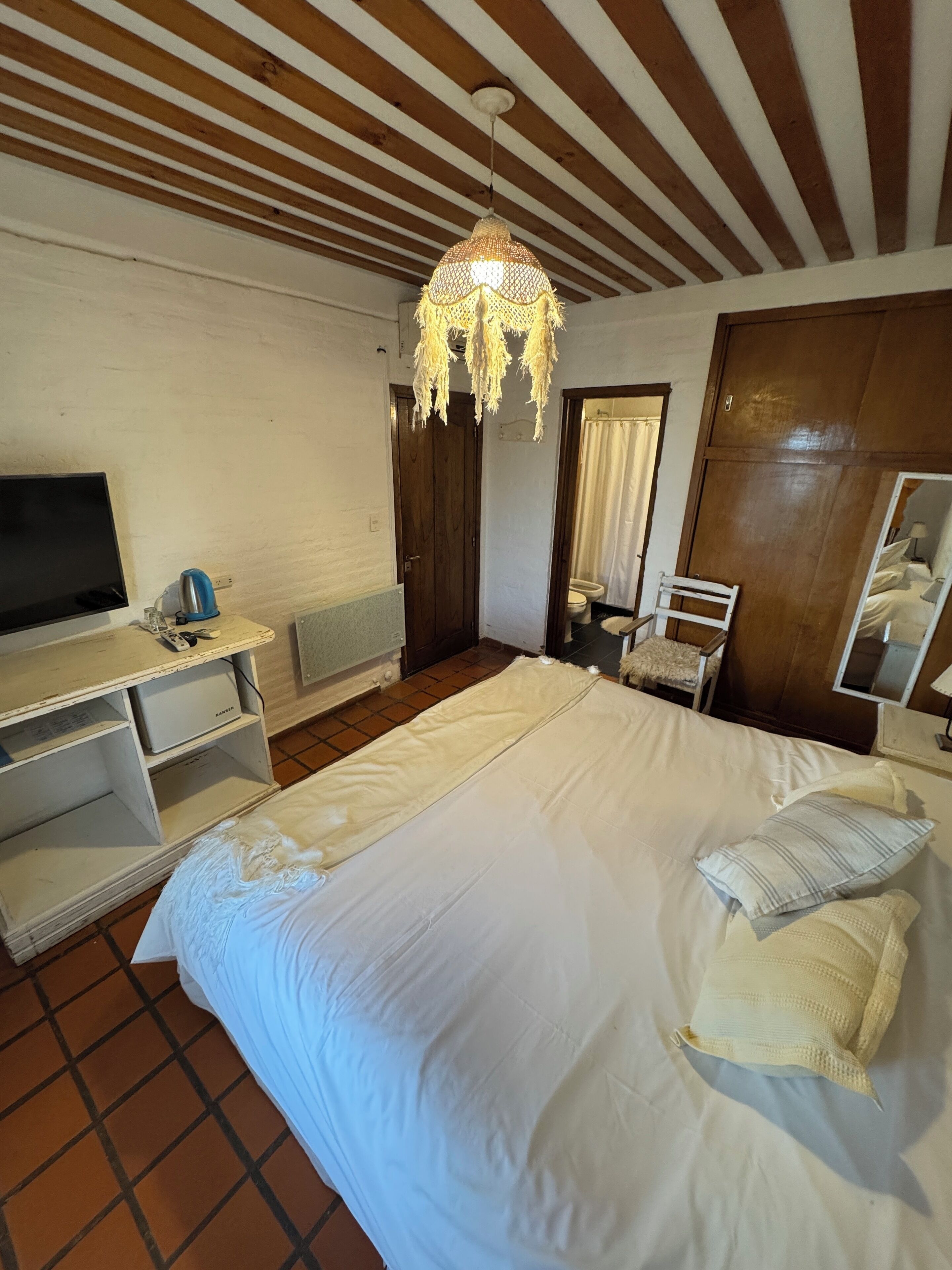 Ein Schlafzimmer mit einem großen Bett, einem Fernseher, einer Holzbalkendecke und einer Pendelleuchte.