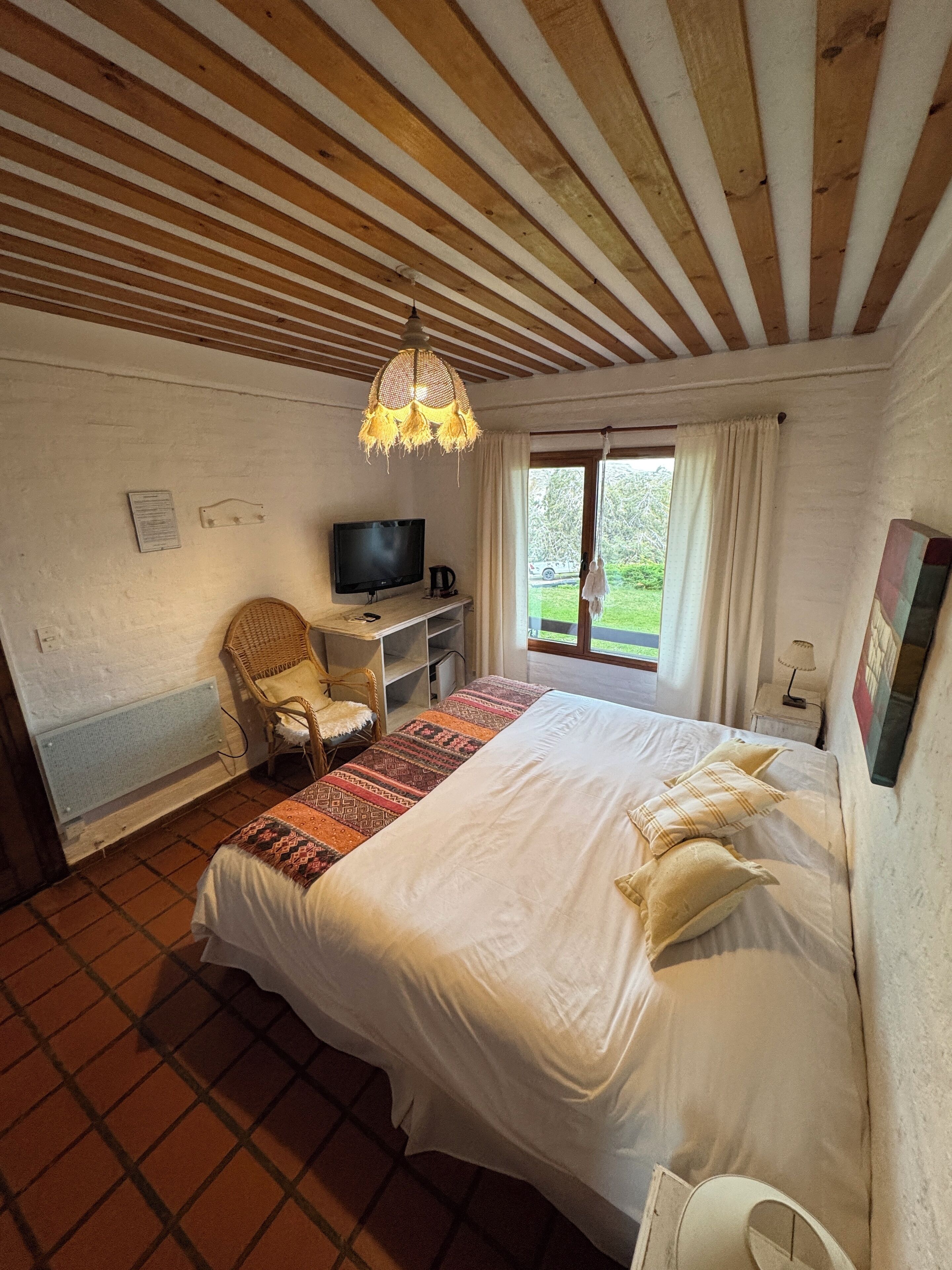 A bedroom with a large bed, a television, a chair, and a window with curtains.